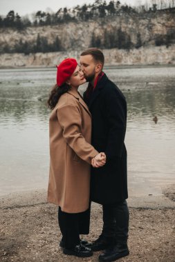 Sevgililer Günü 'nde suyun kenarında el ele tutuşup öpüşen iki kişi. Doğa ve kayalıklarla çevrilidir..