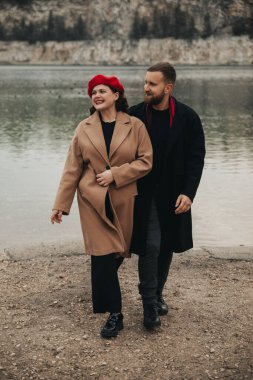 Sevgililer Günü 'nde, sıcak hava için giyinmiş, gülümseyen ve bir anı paylaşan iki kişi kıyıda yürür..