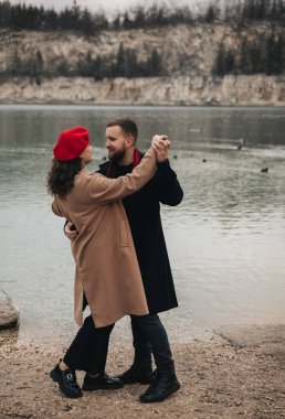 Sevgililer Günü 'nde bir erkek ve kadın su kenarında dans ediyorlar. Bu anın tadını çıkarırken el ele tutuşup gülümsüyorlar..