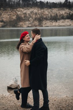 İki insan deniz kenarında yakın bir anın tadını çıkarır. Manzaralı bir kıyı şeridinde kucaklaşırken gülümserler..