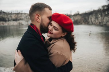 Sevgililer Günü 'nde göl kenarında romantik bir anın tadını çıkaran iki insan. Birbirlerine gülümseyerek sarılıyorlar..