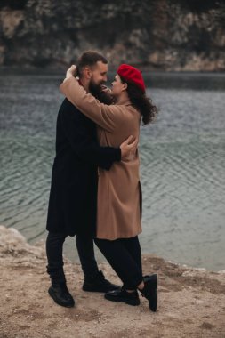 Bir erkek ve kadın, çiftler için özel bir günde birlikte vakit geçirirken bir su kütlesinin yanında sıcak bir kucaklaşmayı paylaşırlar..