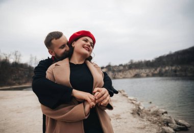 Sevgililer Günü 'nde erkek ve kadın göl kenarında eğleniyor, gülümsüyor ve birbirlerine sarılıyorlar.