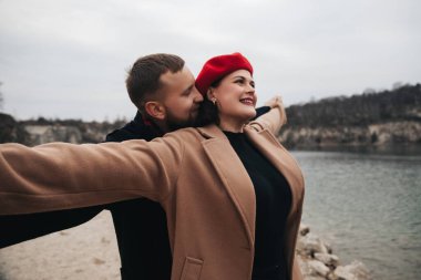 Bir adam bulutlu bir günde suyun kenarında dururken kolları açık bir kadına sarılır. Sevgililer Günü 'nde aşklarını kutluyorlar..