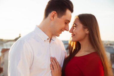 İki insan gün batımında bir anı paylaşır, sıcak bir ışıkla birbirlerine yakın dururlarken yüzlerini aydınlatırlar..