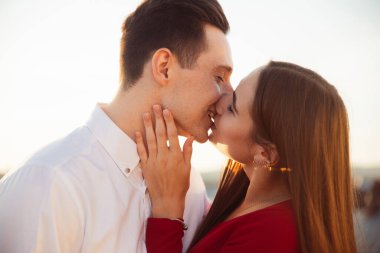 Gün batımında çatıda öpüşen bir çift sıcak bir akşam ışığı ve yumuşak ifadeleriyle sevgisini gösterir..