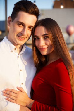 Genç bir çift gün batımında çatıda birbirine yakın durur. Arka planda bir şehir silueti ve üzerinde ışıldayan sıcak bir ışık vardır..