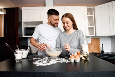 Bir çift mutfakta birlikte yemek tarifi üzerinde çalışıyor. Tezgahta biraz un ve yumurta varken hamuru bir kasede karıştırıyorlar. Yemek pişirmeyi seviyorlar..