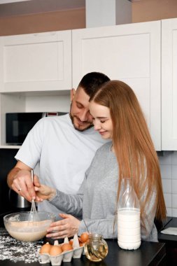 İki kişi mutfakta durmuş, hamuru bir kasede karıştırıyor. Etrafları yumurta, un ve tezgahta bir şişe sütle çevriliyken birbirlerine gülümserler..