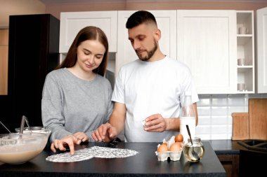 İki kişi bir mutfakta yemek tarifi üzerinde çalışıyor. Malzemelere bakıyorlar ve birlikte yemek yapmak için planlar yapıyorlar. Yumurtalar ve diğer öğeler tezgahta görünür..