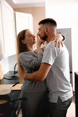 Bir çift yemek pişirirken mutfakta yakın duruyor. Birlikte keyifli bir anı paylaşıyorlar, gülerek ve gülerek akşamları eğleniyorlar..