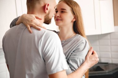 Bir erkek ve kadın bir mutfakta birbirlerine gülümserler. Gündüzleri evlerinde birlikte güzel bir anı paylaşıyorlar..