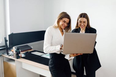 İki kadın, iş görüşmeleri sırasında bir dizüstü bilgisayardaki içeriği inceleyerek bir ofis ortamında iş birliği yapıyor..