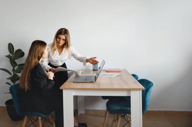 Çalışma ve proje planlamasına odaklanmış iki kadın iş birliği yapıyor ve bir ofis alanında fikirleri paylaşıyor.