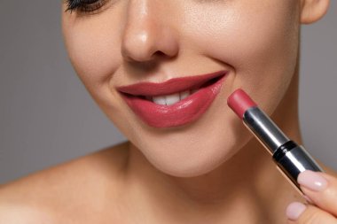 Bir kadın spa ortamında dudaklarına ruj sürerken gülümser ve cilt bakımını yapar..