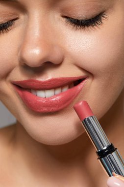 Kadın dudaklarına ruj sürerken gülümsüyor. Günlük cilt bakımını yaparken. Evde iyi aydınlatılmış bir yerde..
