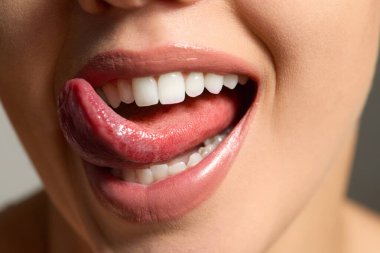 Dudaklarına merhem sürerken nemli dudaklarıyla gülümseyen bir kadın. Yüzüne ve sağlıklı cildine odaklanırken cilt bakımını seviyor..