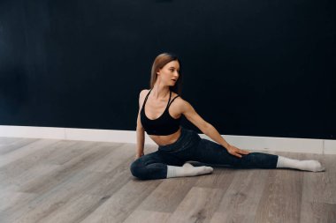 Genç bir kadın, spor yaparken kenarda oturarak egzersiz yapıyor. Basit bir iç mekanda spor yaparken gülümsüyor..