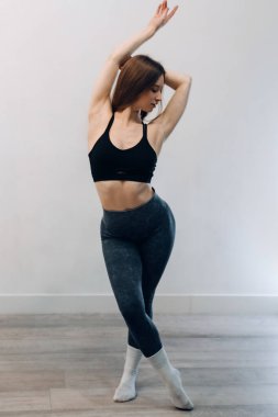 Gülümseyen genç bir dişi, stüdyoda sağlık ve zindelik egzersizi sırasında spor giysileriyle yan esneme hareketleri yapar..