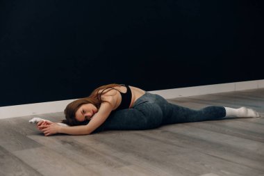 Genç bir bayan spor salonunda yerde spor kıyafetleriyle esneme antrenmanı yapıyor. Spor yapmayı seviyor ve gülümserken sağlıklı bir yaşam tarzını teşvik ediyor..