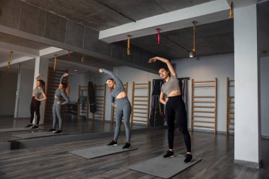 Bir grup kadın spor salonunda ısınma egzersizleri yapıyor, esneme ve esnekliğe odaklanıyor..