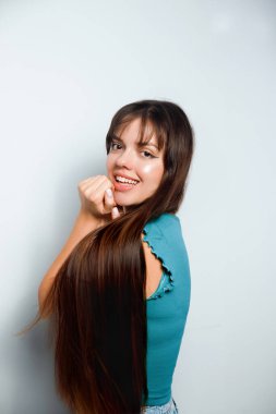 Genç kız arka planda duruyor, uzun saçlarını tutarken gülümsüyor ve gündüzleri iki elini de kapalı tutuyor..