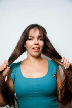 Bir kadın uzun saçlarını içeride çekerken gülümsüyor. Arkaplan açık ve basit, ifadesine odaklanıyor..