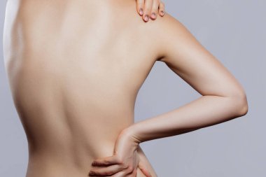 Sağ eli omzunda dururken bir kadın stüdyoda sol eliyle belini tutuyor..