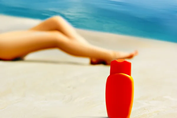 Пляшка сонячного блоку і жіноче нанесення крему на ногу — стокове фото