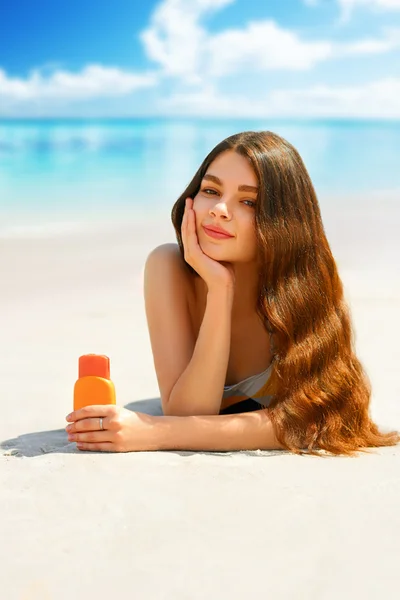 Portret przepiękny młoda kobieta uśmiechając się relaks na plaży i trzymając butelkę ochrony przeciwsłonecznej — Zdjęcie stockowe