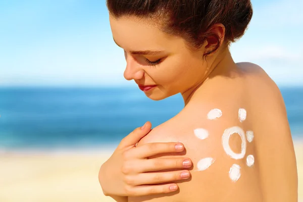 Porträtt av vackra unga kvinnan ler i bikini med ritade solen på axeln på stranden — Stockfoto