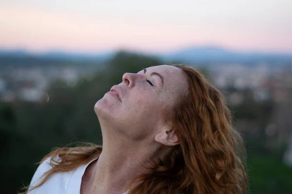 50 yaşında, beyaz tişörtlü, çok hassas ve rahatlatıcı yüzlü kızıl saçlı bir kadın..