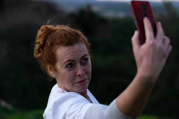 50 yaşında, beyaz tişörtlü, çok hassas ve rahatlatıcı yüzlü kızıl saçlı bir kadın..