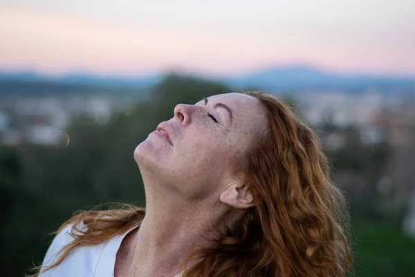 50 yaşında, beyaz tişörtlü, çok hassas ve rahatlatıcı yüzlü kızıl saçlı bir kadın..