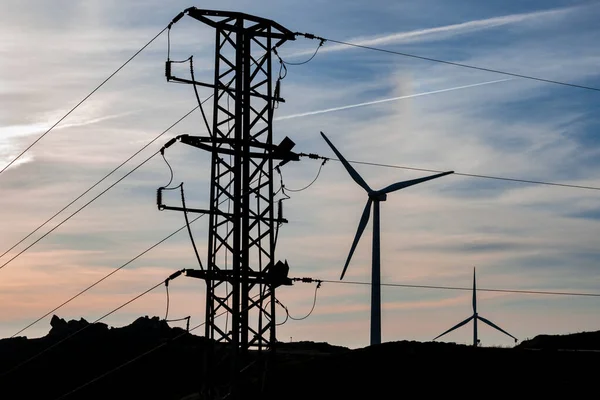 Gün batımında çekilen sahnede yüksek voltaj kulesi olan eolik park.