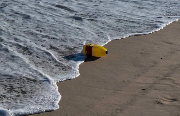 Sahilde dalgalarla yıkanmış bir şişe sarı çamaşır suyu.