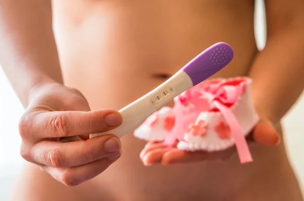 Donna con scarpe da bambino e test di gravidanza positivo — Foto Stock