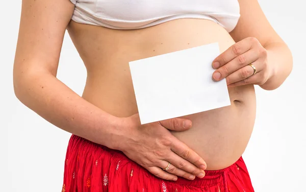 Barriga de uma mulher grávida com um papel branco em branco — Fotografia de Stock