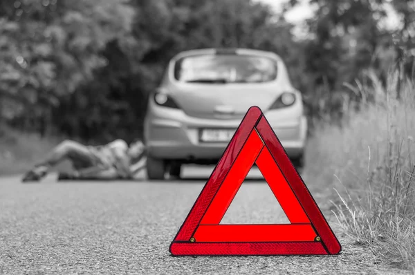 तुटलेली कार आणि लाल त्रिकोण अंतर्गत पडलेला ड्रायव्हर — स्टॉक फोटो, इमेज