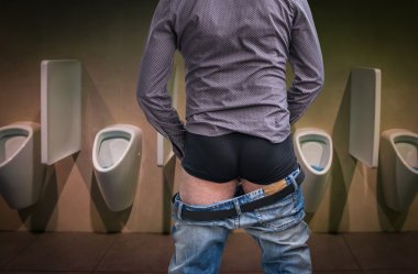 Standing man peeing to a urinal in restroom clipart