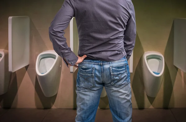 Standing man peeing to a urinal in restroom — Stock Photo, Image