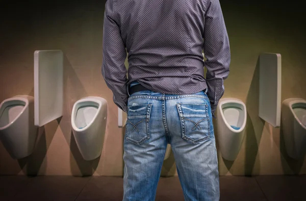 Стоячий мужчина писает в туалет перед писсуаром — стоковое фото
