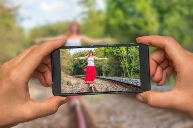 Taking photo of lady walking on railway with mobile phone clipart