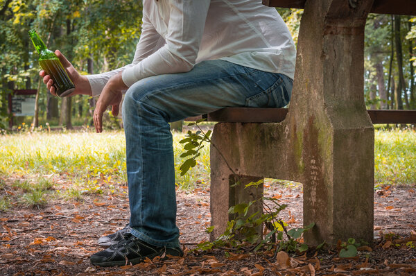 Депрессивный пьяница с бутылкой пива сидит на скамейке
