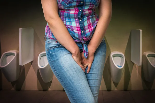 Mulher com as mãos segurando sua virilha no banheiro público dos homens — Fotografia de Stock