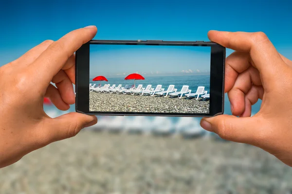 Toma de fotos de tumbonas y sombrillas rojas con teléfono celular — Foto de Stock