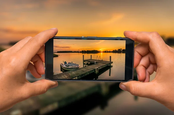 Tomar una foto de la puesta de sol sobre el lago con teléfono móvil — Foto de Stock