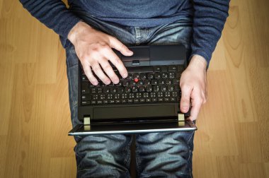 Dizüstü bilgisayar kullanarak ve ahşap katta oturan genç öğrenci