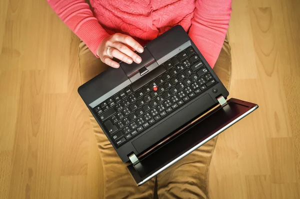 Молодий студент використовує ноутбук і сидить на дерев'яній підлозі — стокове фото