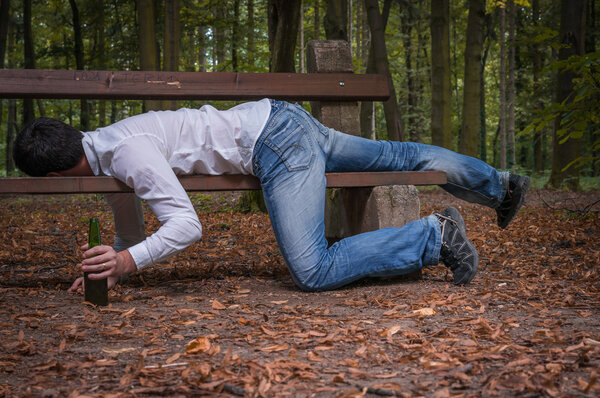 Пьяный мужчина спит на скамейке в парке с пивными бутылками
